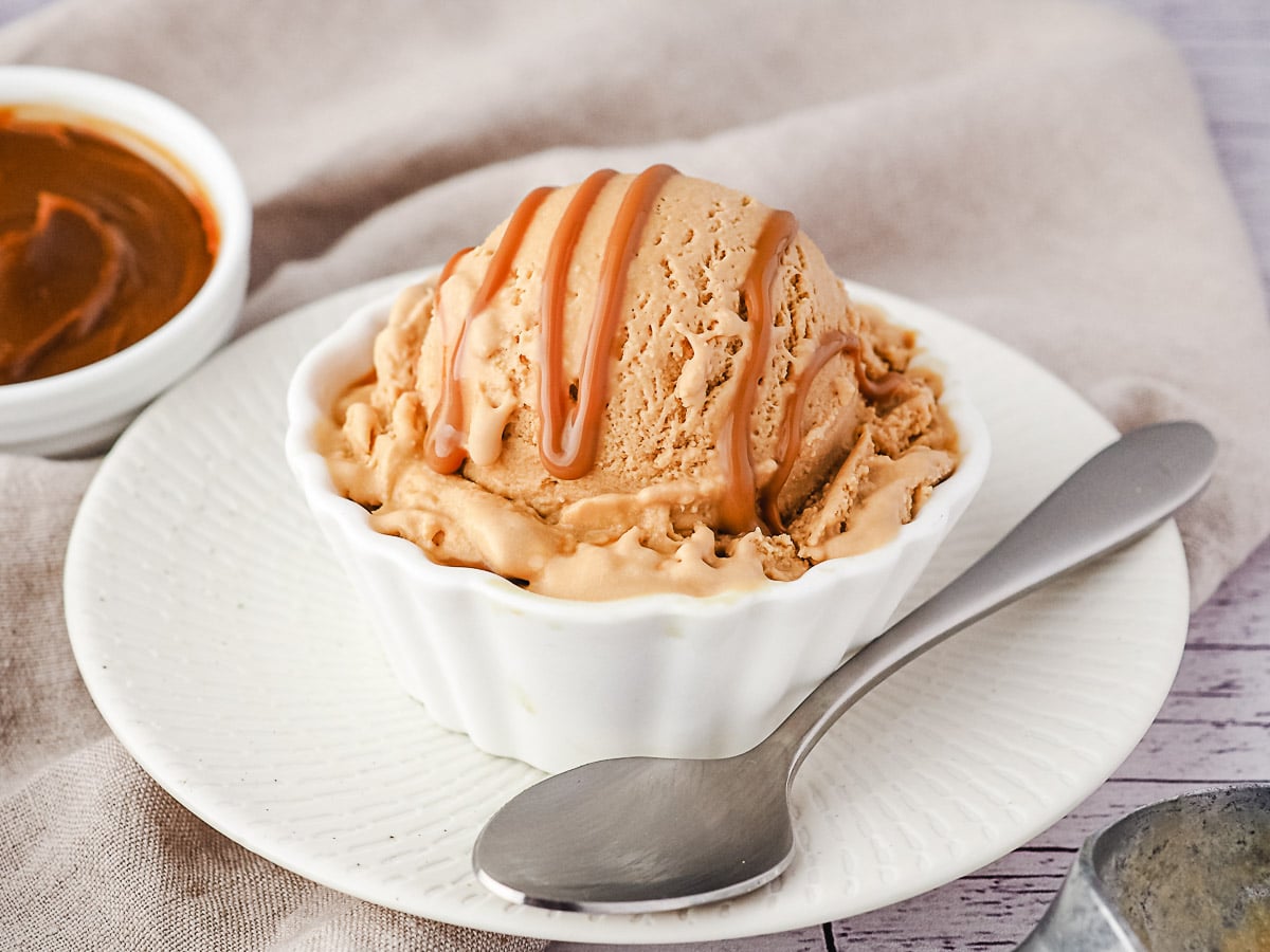 Scoop of ice cream with dulce de leche drizzle and dulce de leche in background.