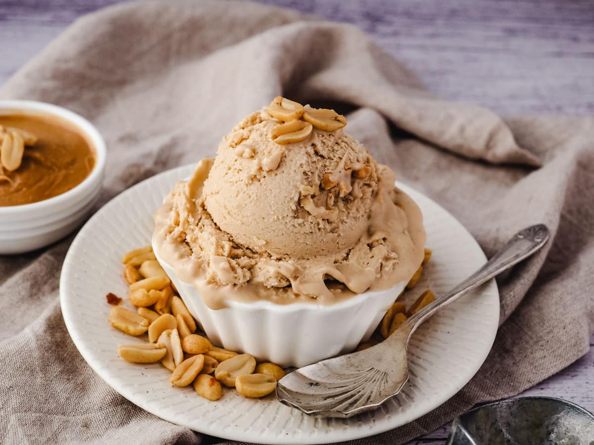 Scoop of ice cream in a bowl with roasted peanuts, and a spoon on the side.