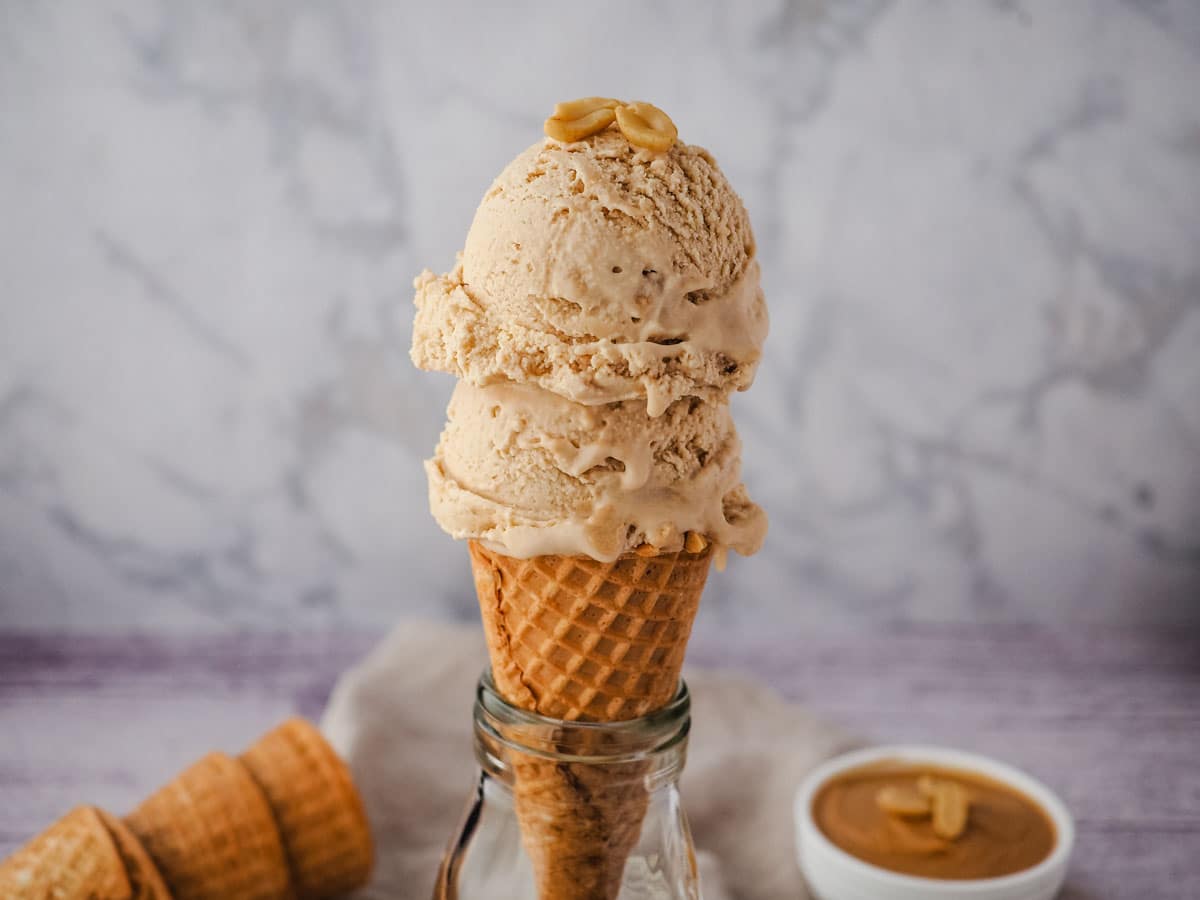 Peanut Butter Ice Cream 3 Two scoops of ice cream in a cone with roasted peanuts on top.