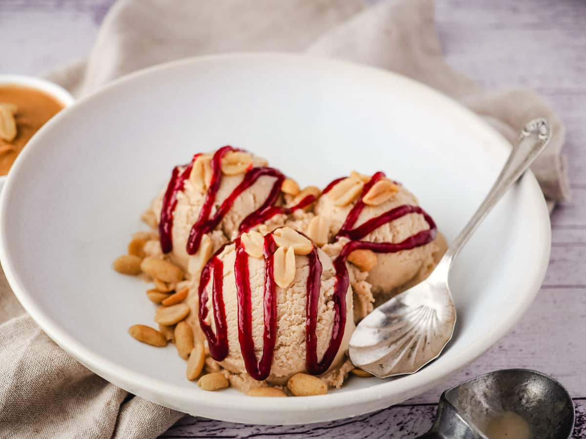 Scoops of peanut butter ice cream drizzled with raspberry jam in a bowl.