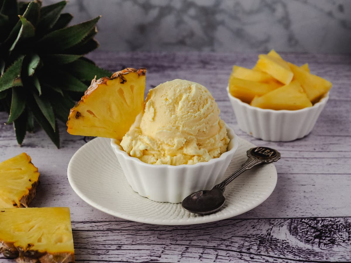 Pineapple Ice Cream 8 Scoop of ice cream in a bowl, garnished with fresh pineapple and fresh pineapple in the background.
