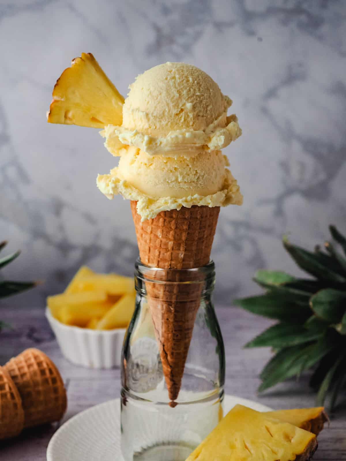Pineapple Ice Cream 11 Two scoops of ice cream in a cone garnished with fresh pineapple, with fresh pineapple in the background.