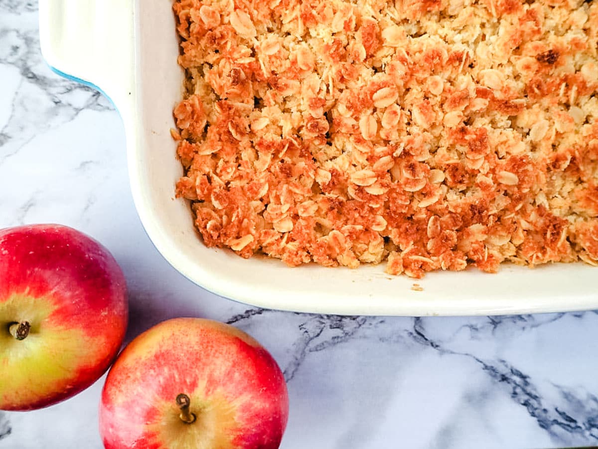 Baking dish of apple crumble with fresh apples on the side.