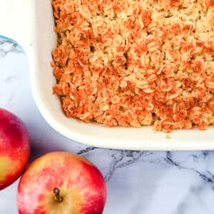 Baking dish of apple crumble with fresh apples on the side.