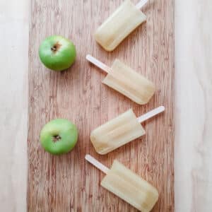 Easy apple popsicles 3 Apple popsicles on a board with fresh apples.