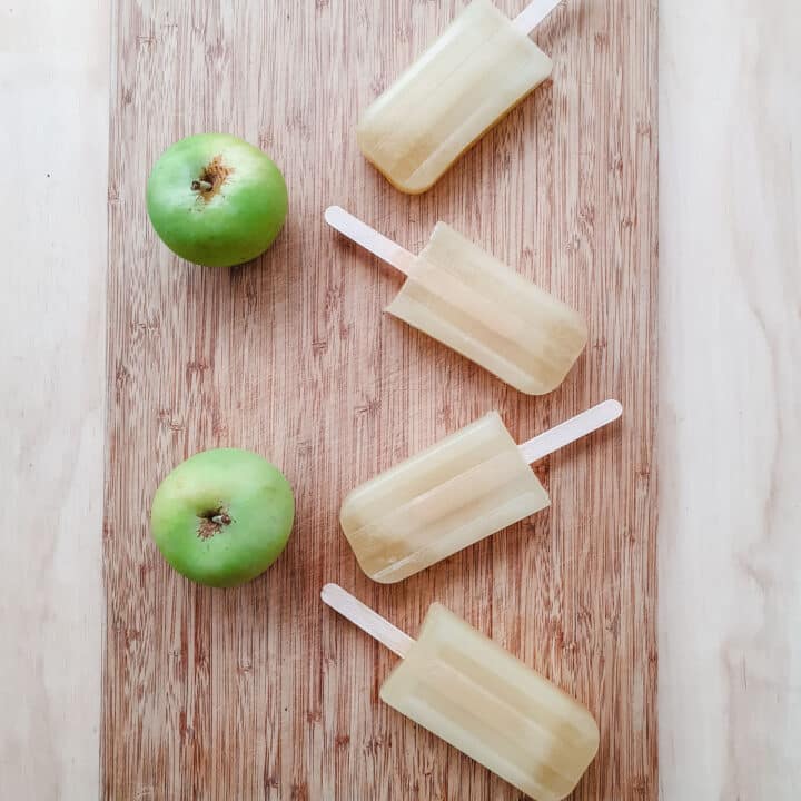 Apple popsicles on a board with fresh apples.