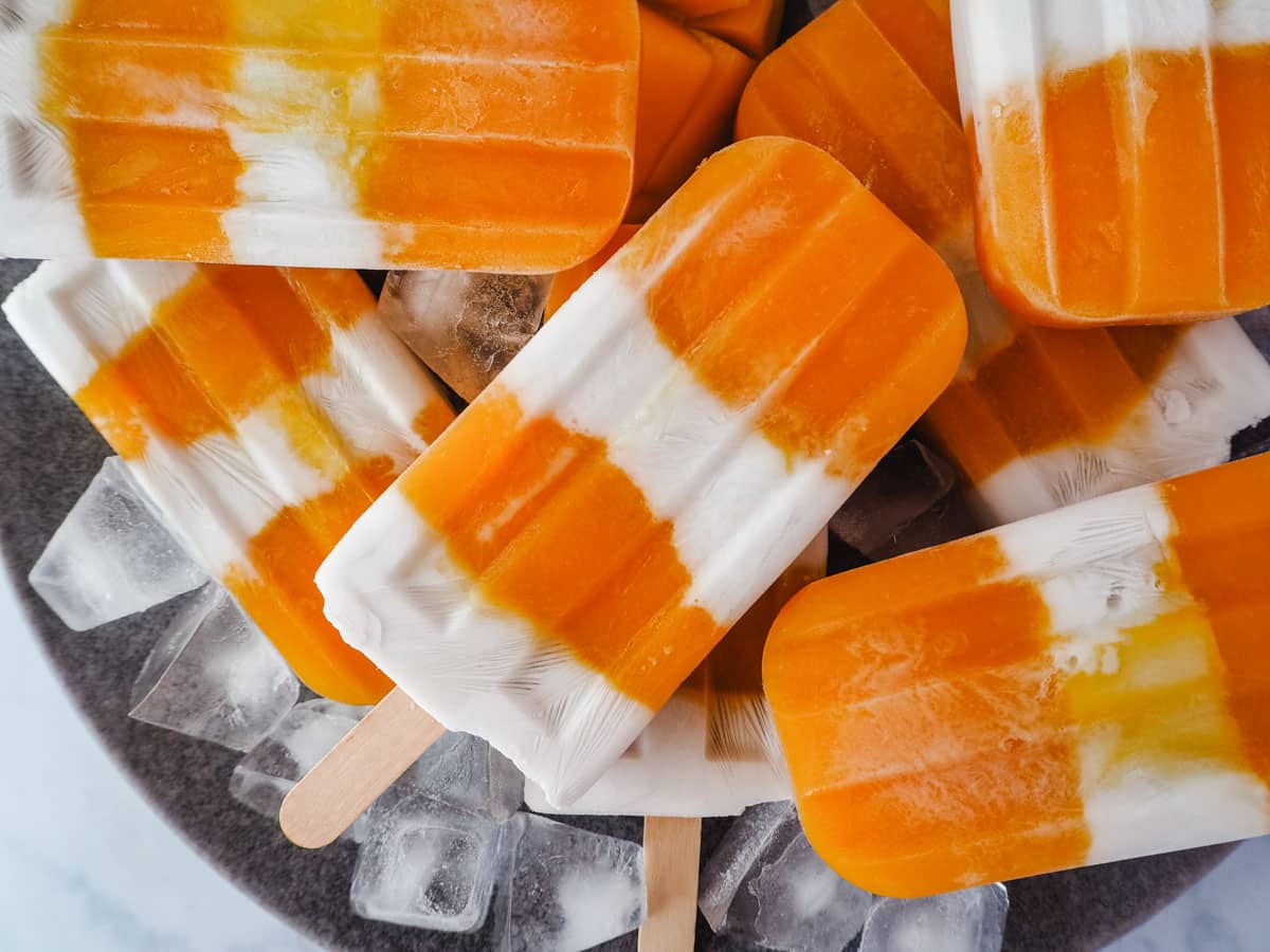 Pile of mango coconut popsicles in a bowl with ice.