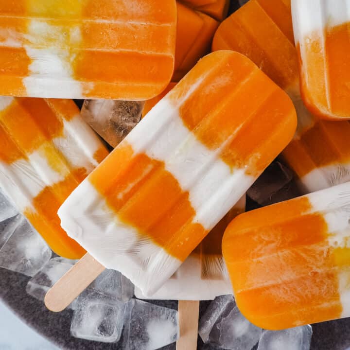 Pile of mango coconut popsicles in a bowl with ice.