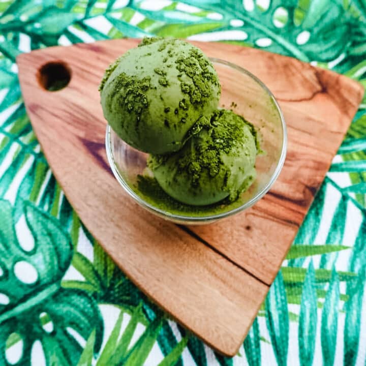Close up two scoops of matcha ice cream sprinkled with matcha powder.