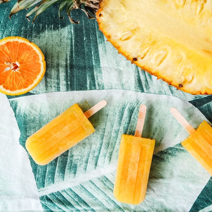Pineapple, orange and ginger popsicles with fresh pineapple and orange in the background.