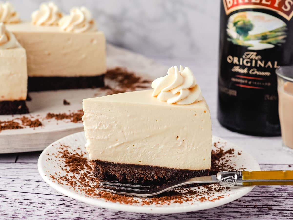 Baileys cheesecake on a plate with cheesecake and Baileys in the background.