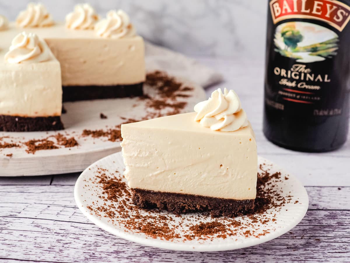 No bake Baileys cheesecake on a plate with cheesecake and Baileys in the background.