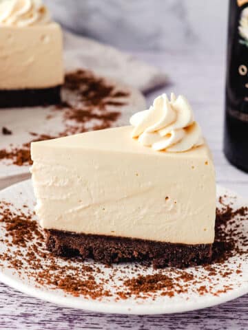 Baileys cheesecake on a plate with cheesecake and Baileys in the background.