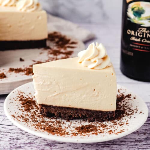 Baileys cheesecake on a plate with cheesecake and Baileys in the background.