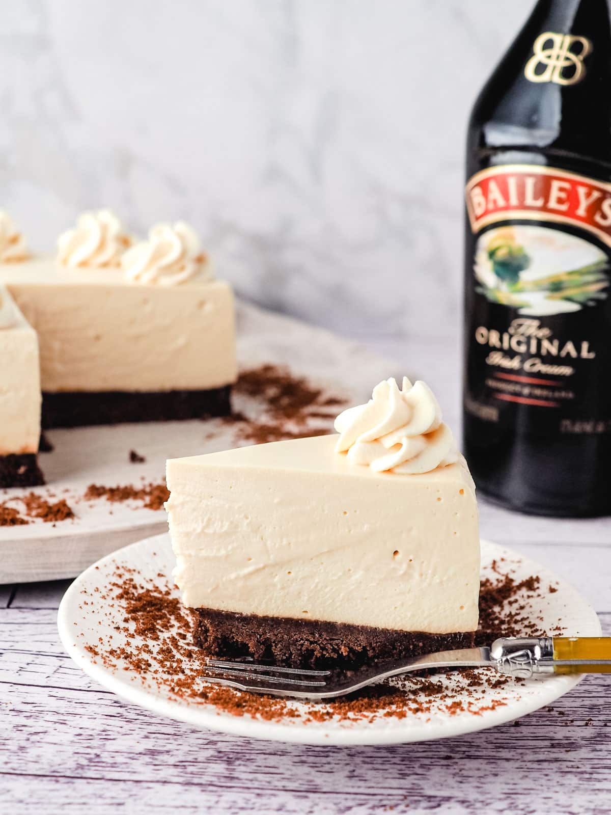 Baileys cheesecake on a plate with cheesecake and Baileys in the background.