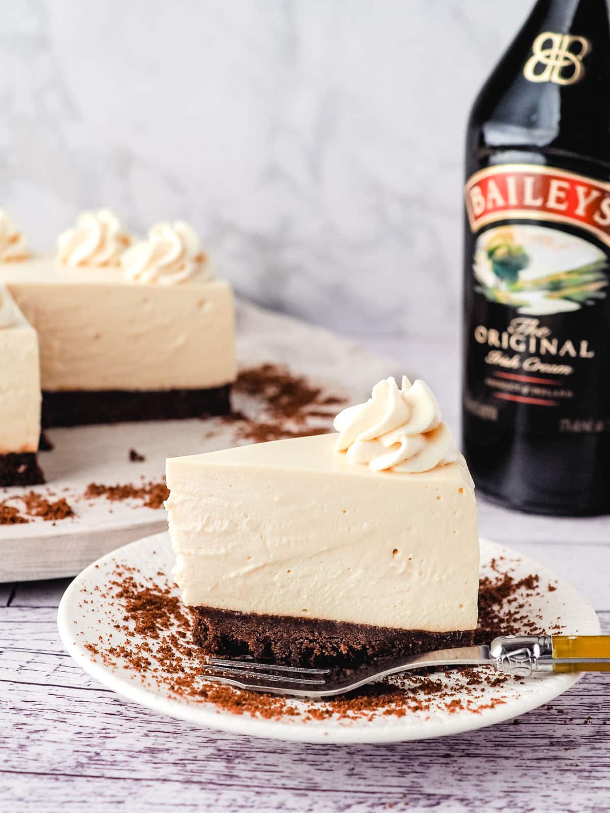 No Bake Baileys Cheesecake 13 Baileys cheesecake on a plate with cheesecake and Baileys in the background.