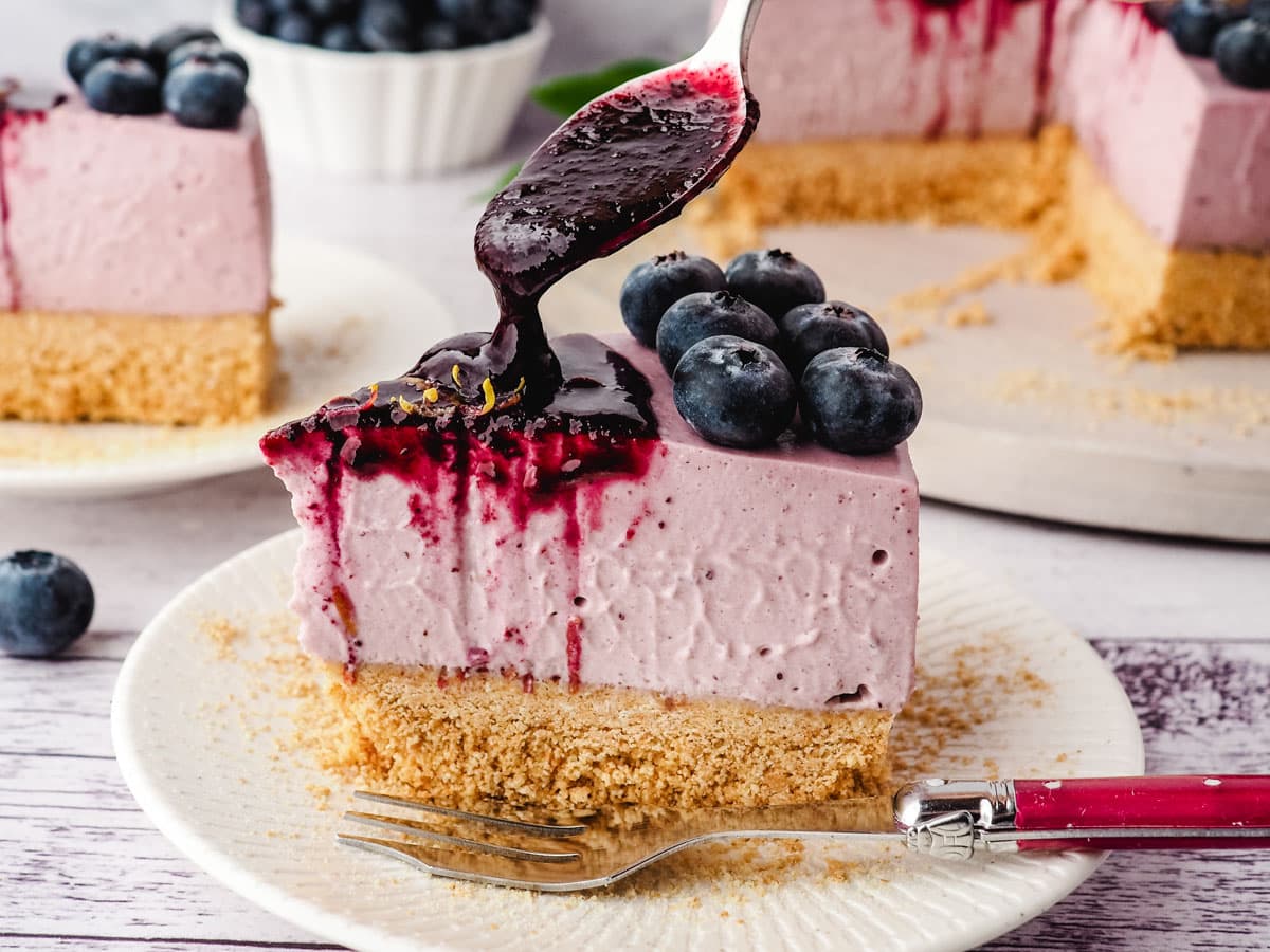 Blueberry topping being spooned onto a slice of no bake blueberry cheesecake.