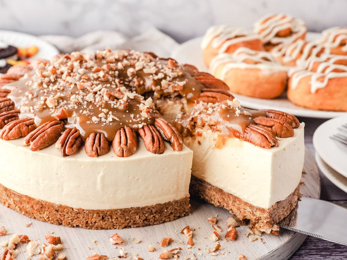 Serving caramel pecan cheesecake, with Thanksgiving desserts in the background.