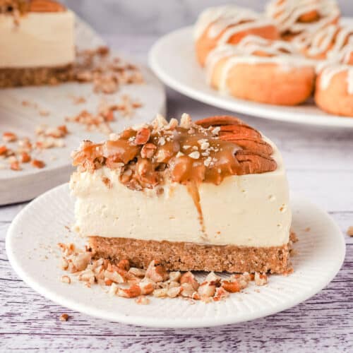 Slice of caramel pecan cheesecake on a plate, with rest of cheesecake, and a plate of air fryer cinnamon scrolls in the background.