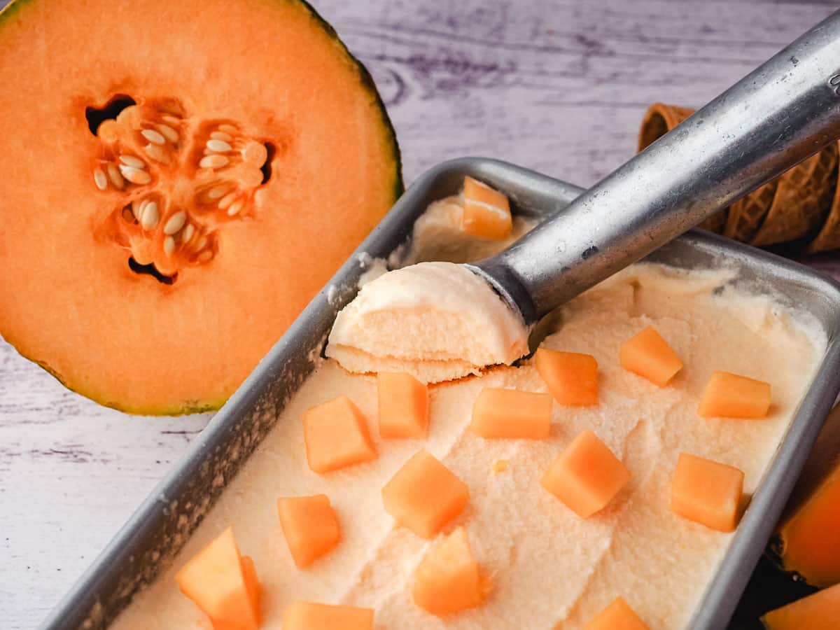 Scooping melon ice cream from a tin, with fresh melon in the background.