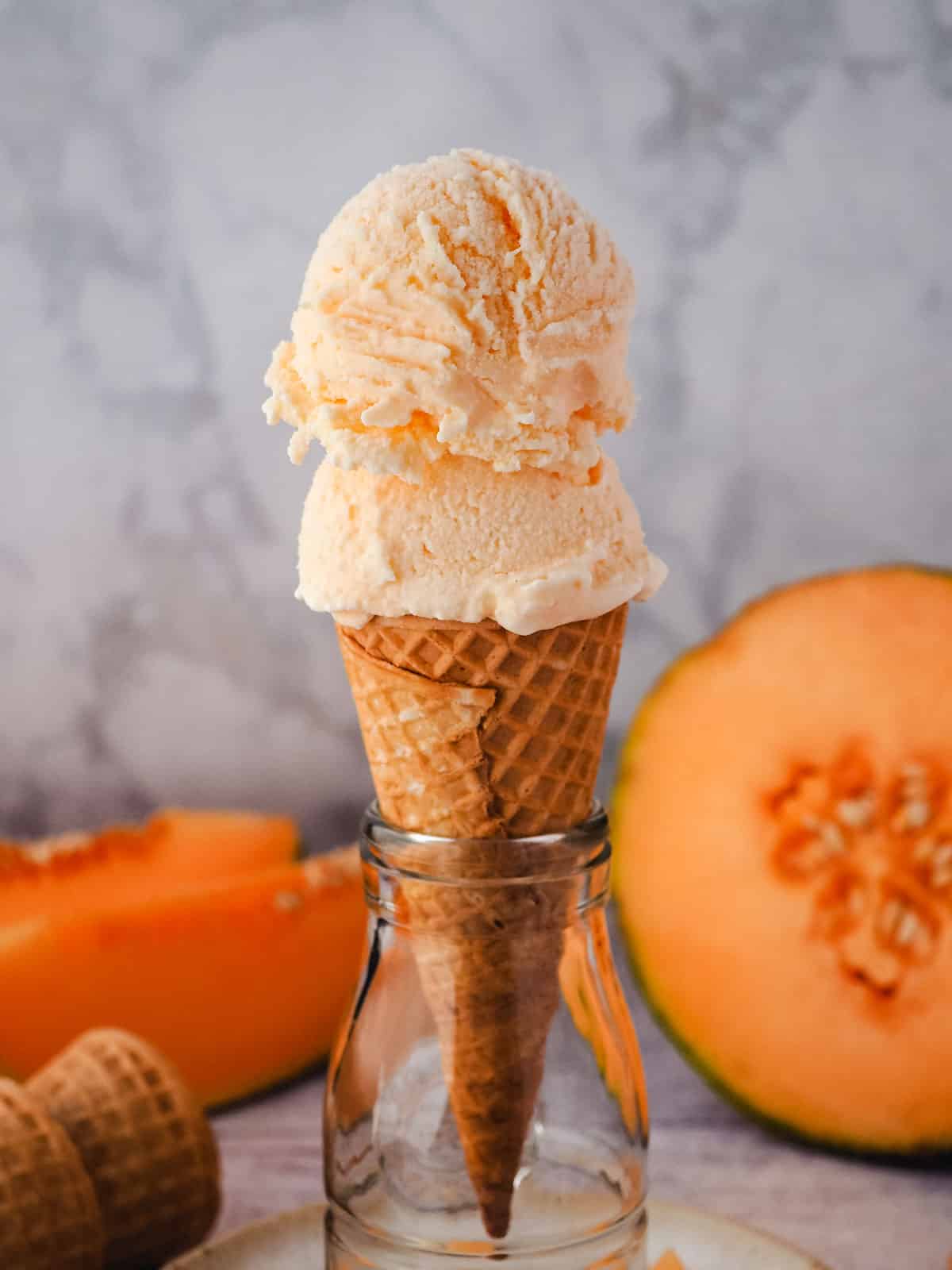 Melon Ice Cream 11 Two scoops of melon ice cream in a cone, with fresh melon in the background.