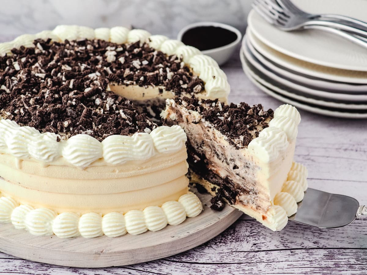 Slicing Oreo ice cream cake with a stack of forks in the background.