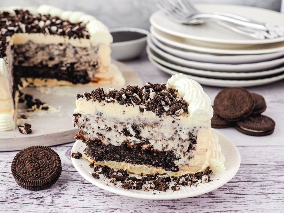 Slice of Oreo ice cream cake, with rest of cake in background and stack of forks.