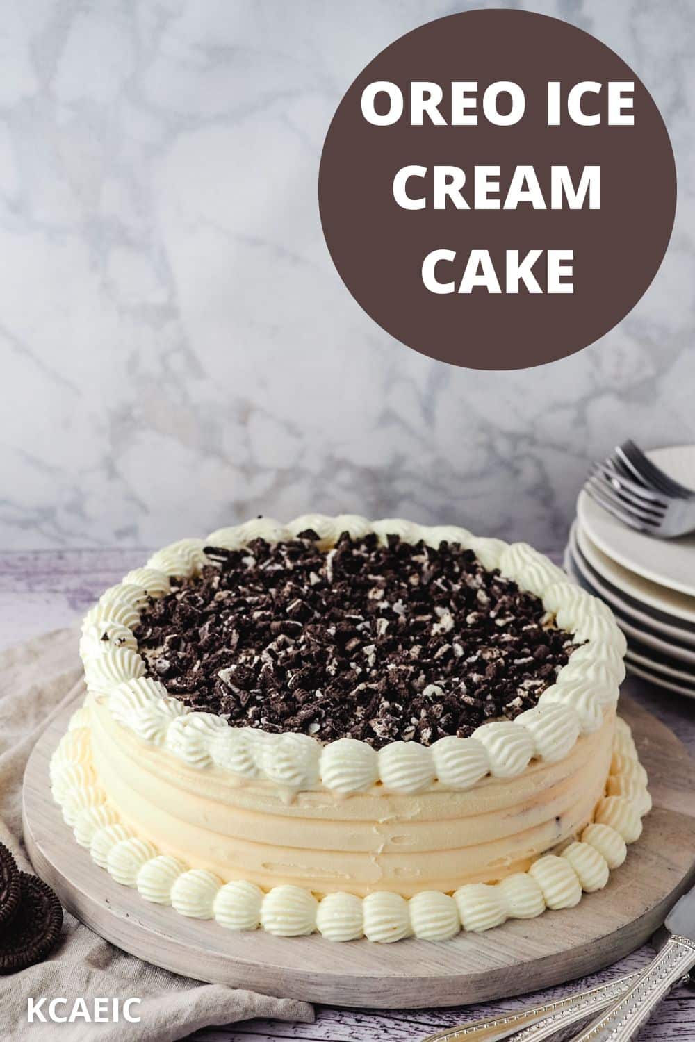 Whole Oreo ice cream cake on a serving platter, with stack of plates in the background.