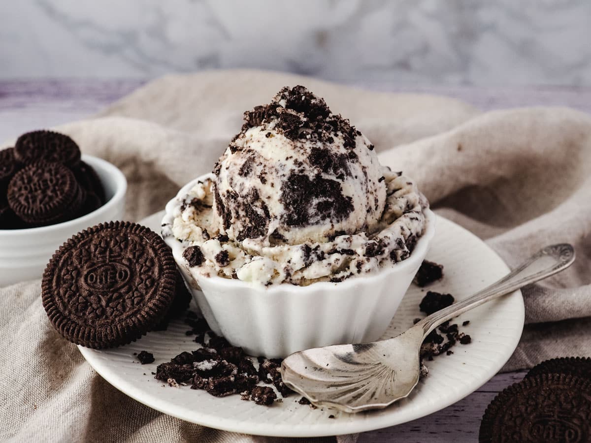 Scoop of Oreo ice cream in a bowl, sprinkled with crushed up Oreos, with more Oreos on the side.