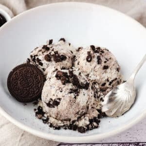 Three scoops of Oreo ice cream in a bowl with a spoon.