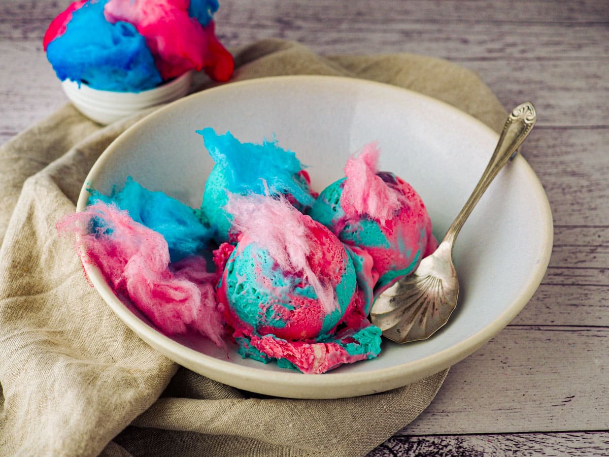 Scoops of pink and blue cotton candy ice cream garnished with cotton candy.