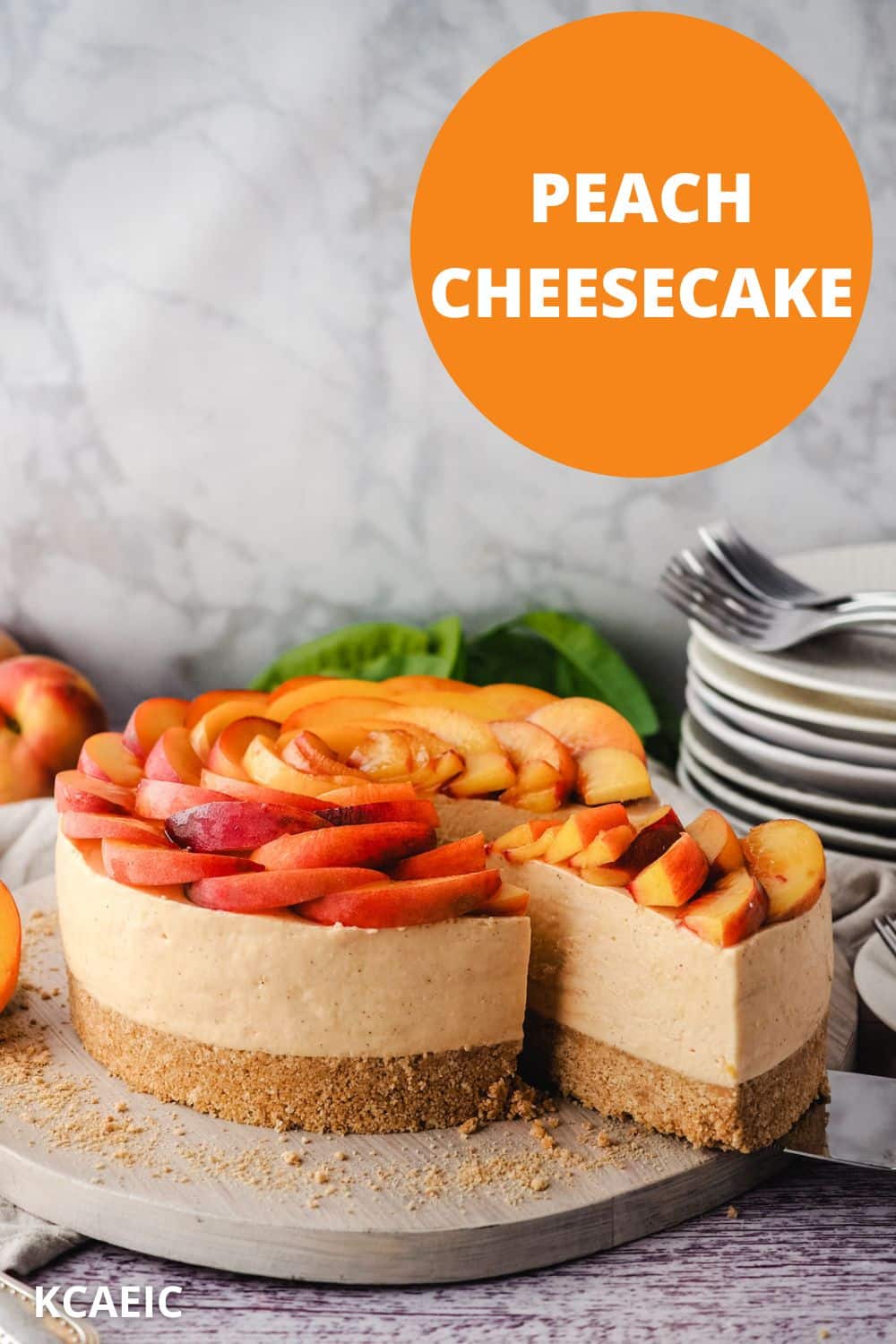 Removing a slice of peach cheesecake from the cake, with a pile of plates and forks in the background and text overlay, peach cheesecake and KCAEIC.