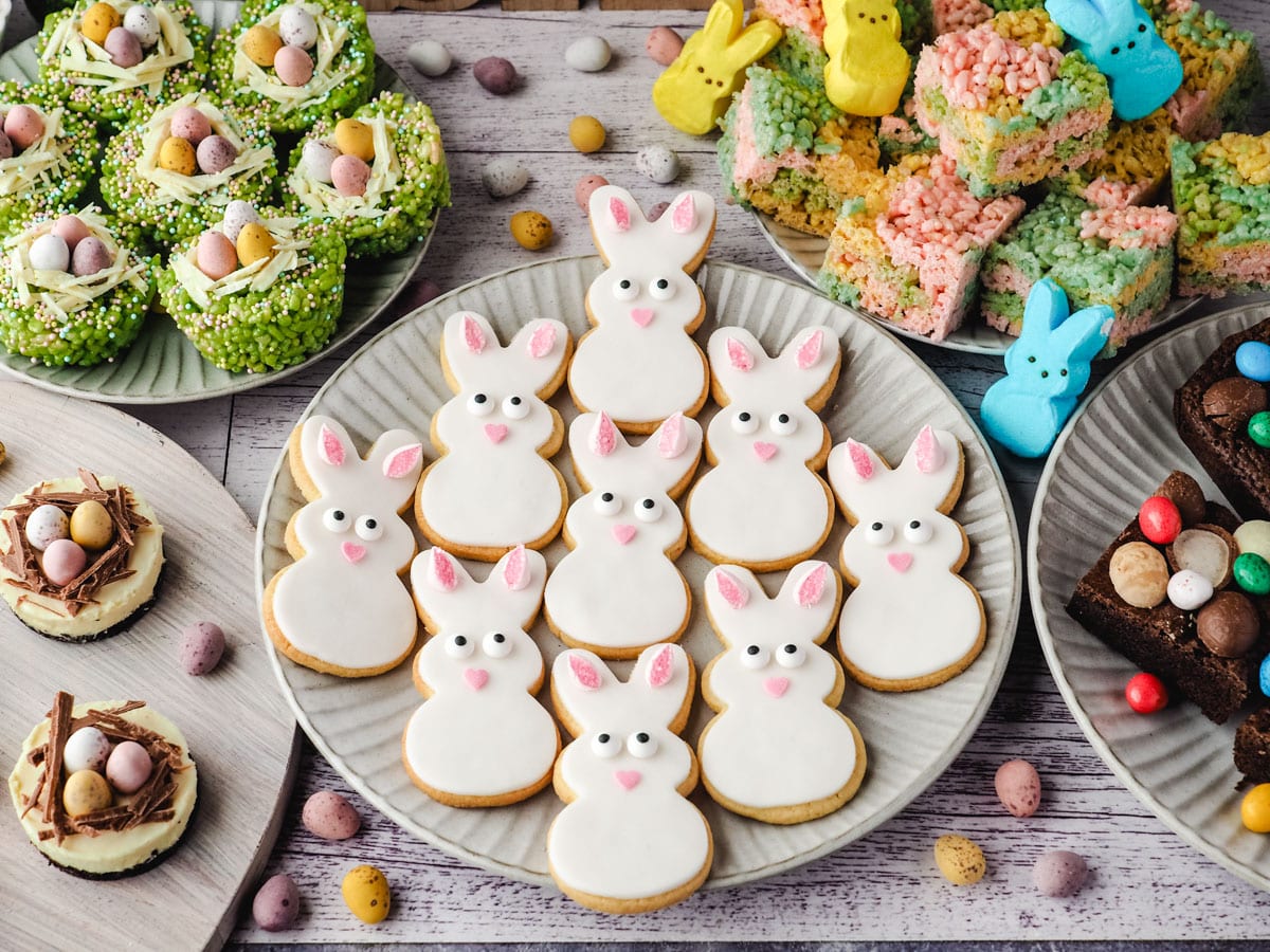 Bunny cookies on a plate surrounded by Easter desserts and decorations.