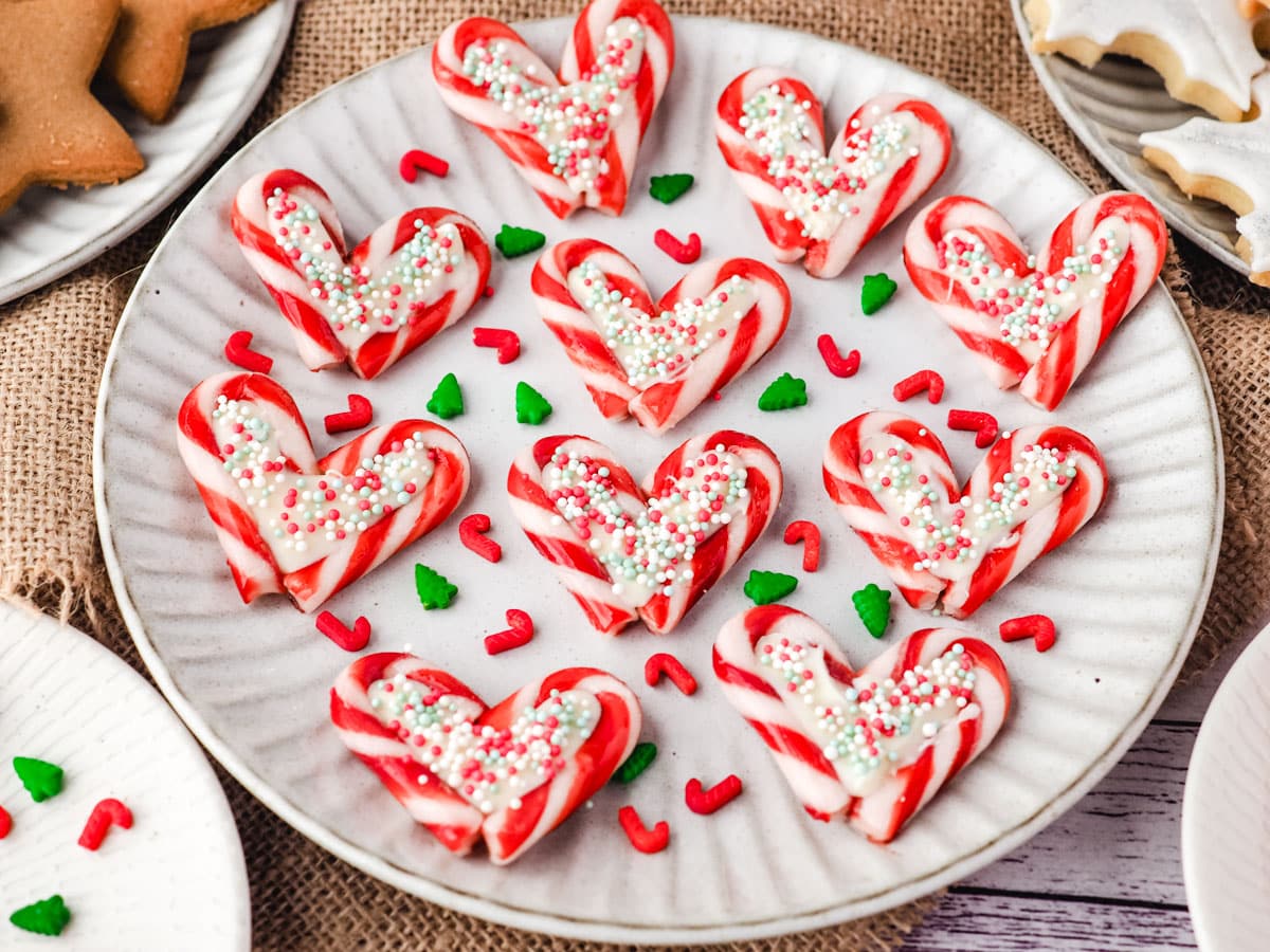 Candy cane hearts on a plate with sprinkles, on a Christmas dessert table.