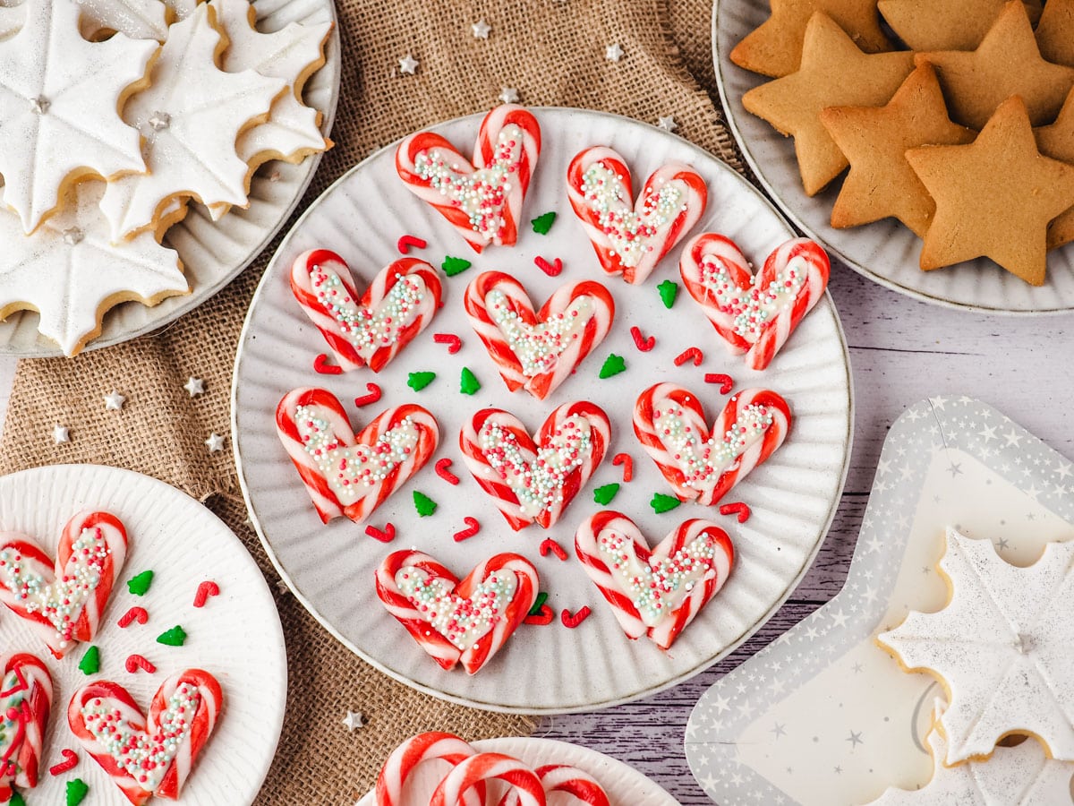 Candy cane hearts on a plate with sprinkles, on a Christmas dessert table.