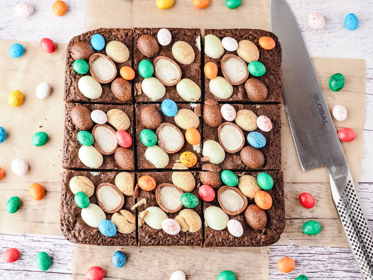 Top down shot of sliced Easter brownies with a knife on the side, surrounded by extra Easter eggs.