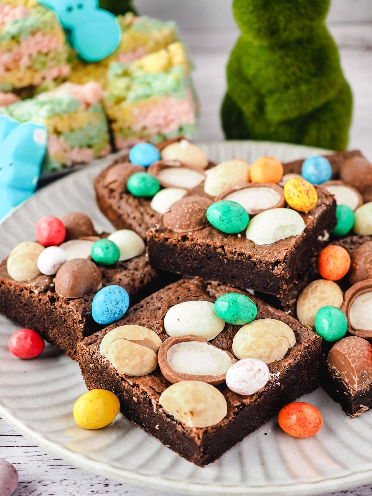 Easter brownies decorated with Easter eggs on a plate, with Easter decorations in the background.