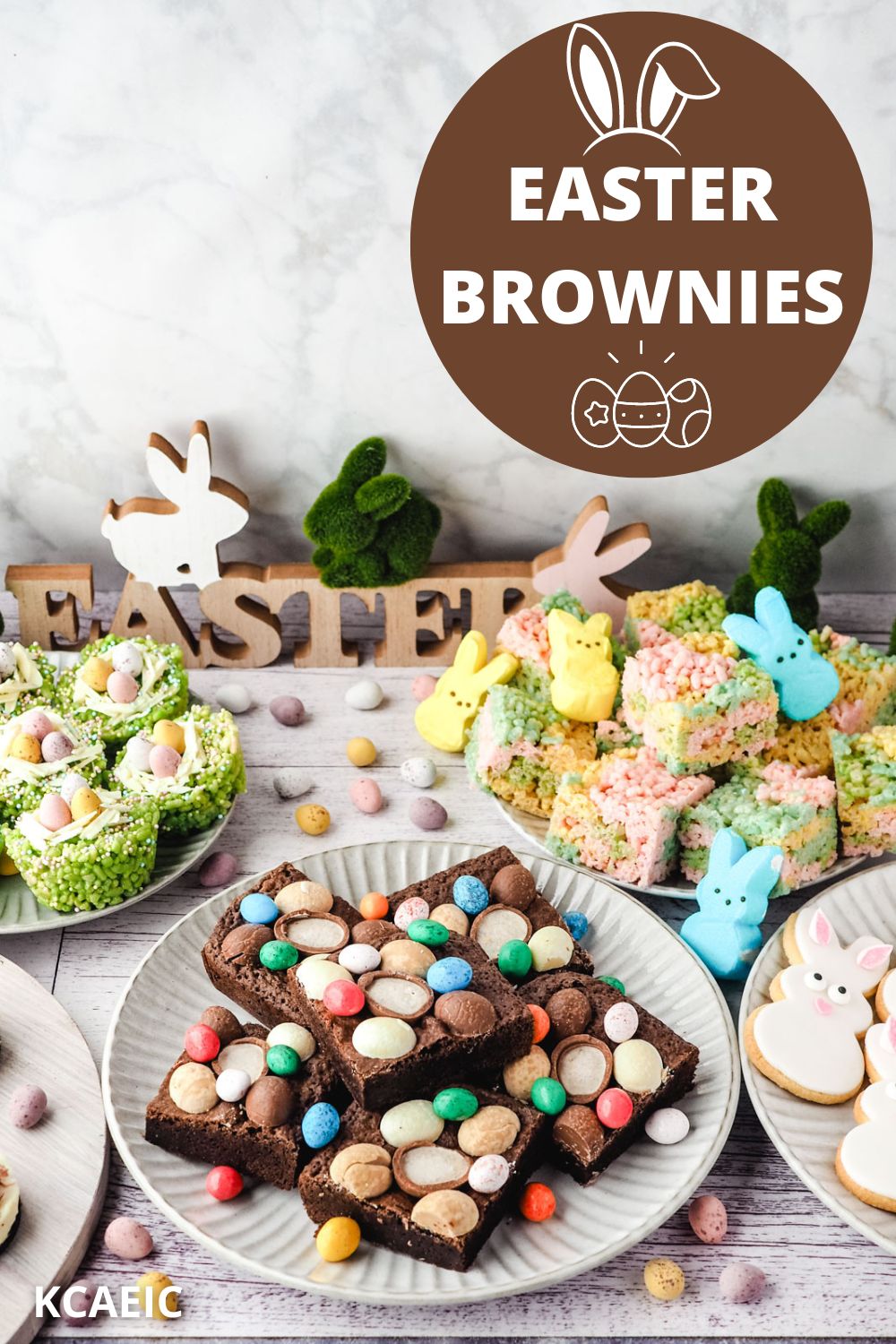 Easter brownies decorated with Easter eggs on a plate, on an Easter dessert table with bunny cookies, Easter rice krispie treats and peeps rice krispie treats in the background.