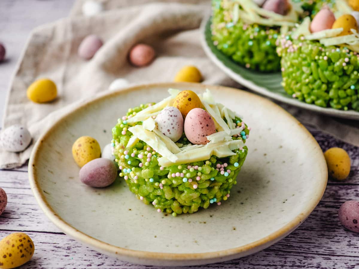 Easter rice krispie treats on a plate with mini eggs on the side and rest of rice krispie treats on a plate next to it.