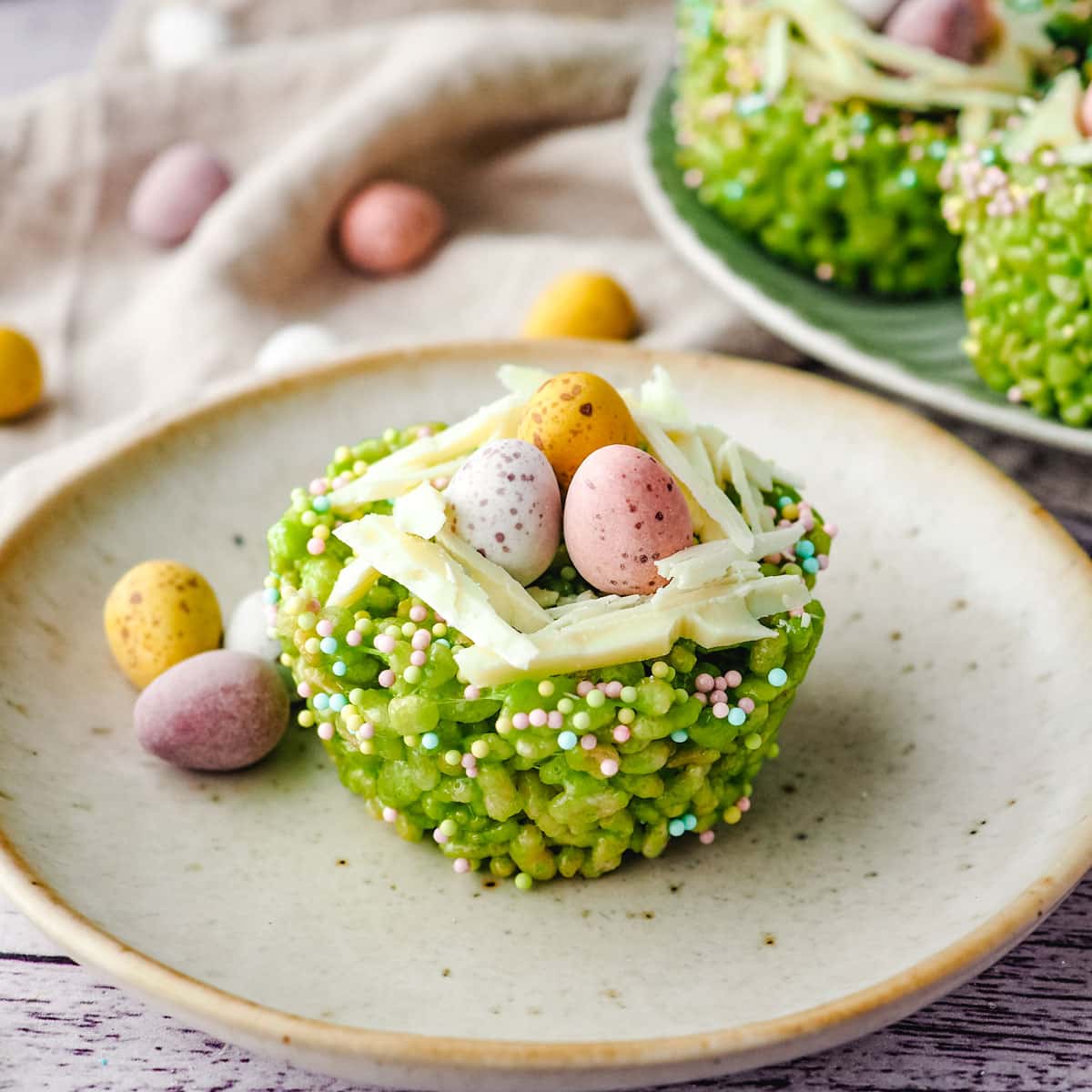 Easter rice krispie treats on a plate with mini eggs on the side and rest of rice krispie treats on a plate next to it.