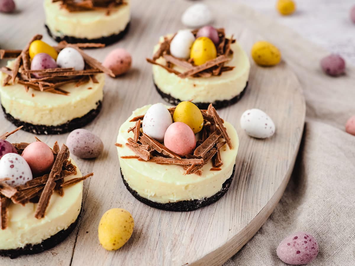 Mini egg cheesecakes on a serving board with extra mini eggs.