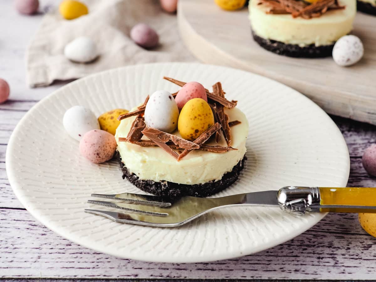 Mini egg cheesecake on a plate with a fork and extra mini eggs on the side.