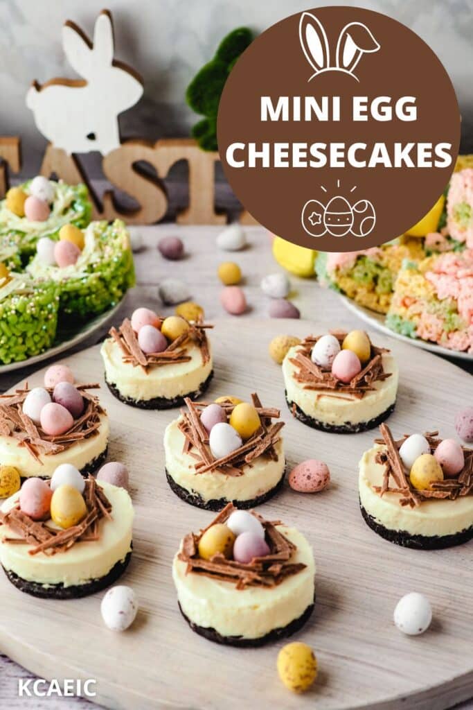 Mini egg cheesecakes on a serving board with Easter desserts and decorations in the background.
