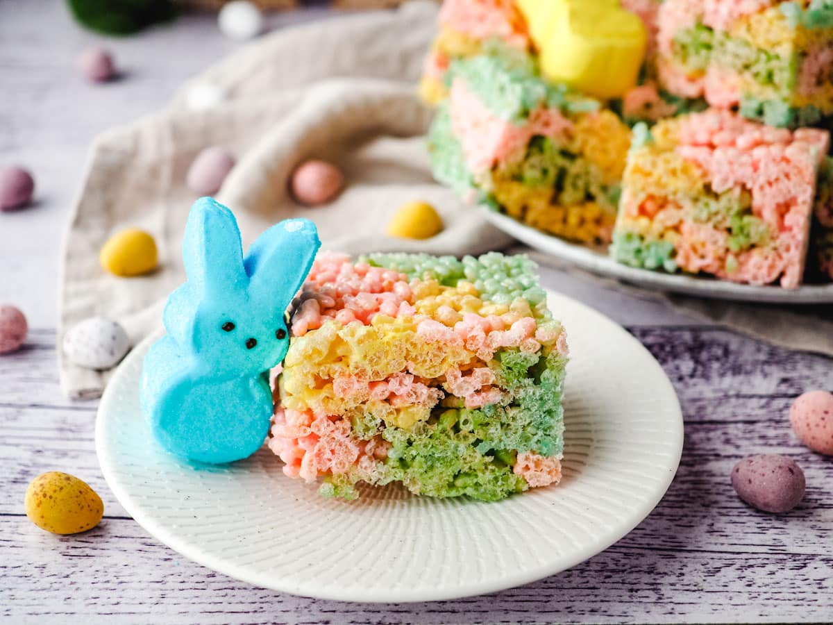 Peeps rice krispie treat on a plate with a Peep on the side and plate with rest of treats in the background.