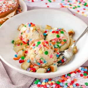 Scoops of birthday cake ice cream in a bowl with a spoon, surrounded by sprinkles.