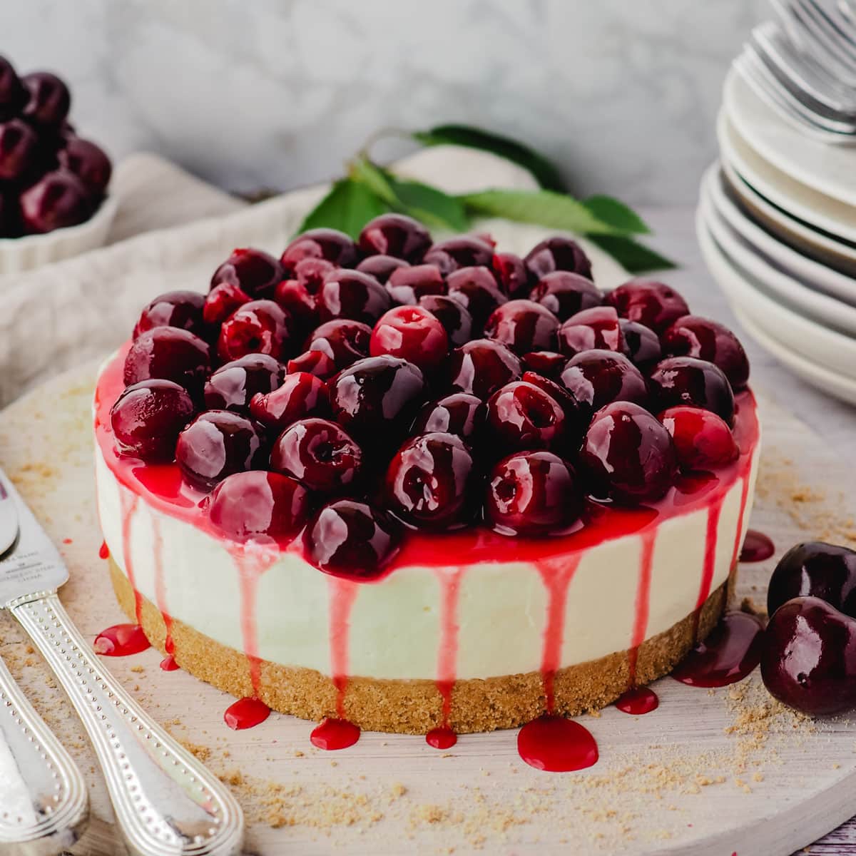 Cherry cheesecake on a serving platter with fresh cherries and serving ware on the side.