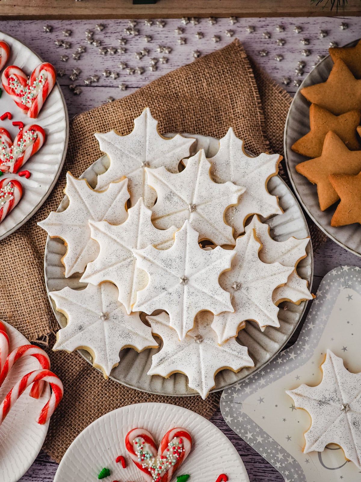 Snowflake cookies on a plate surrounded by Christmas desserts and Christmas decorations.