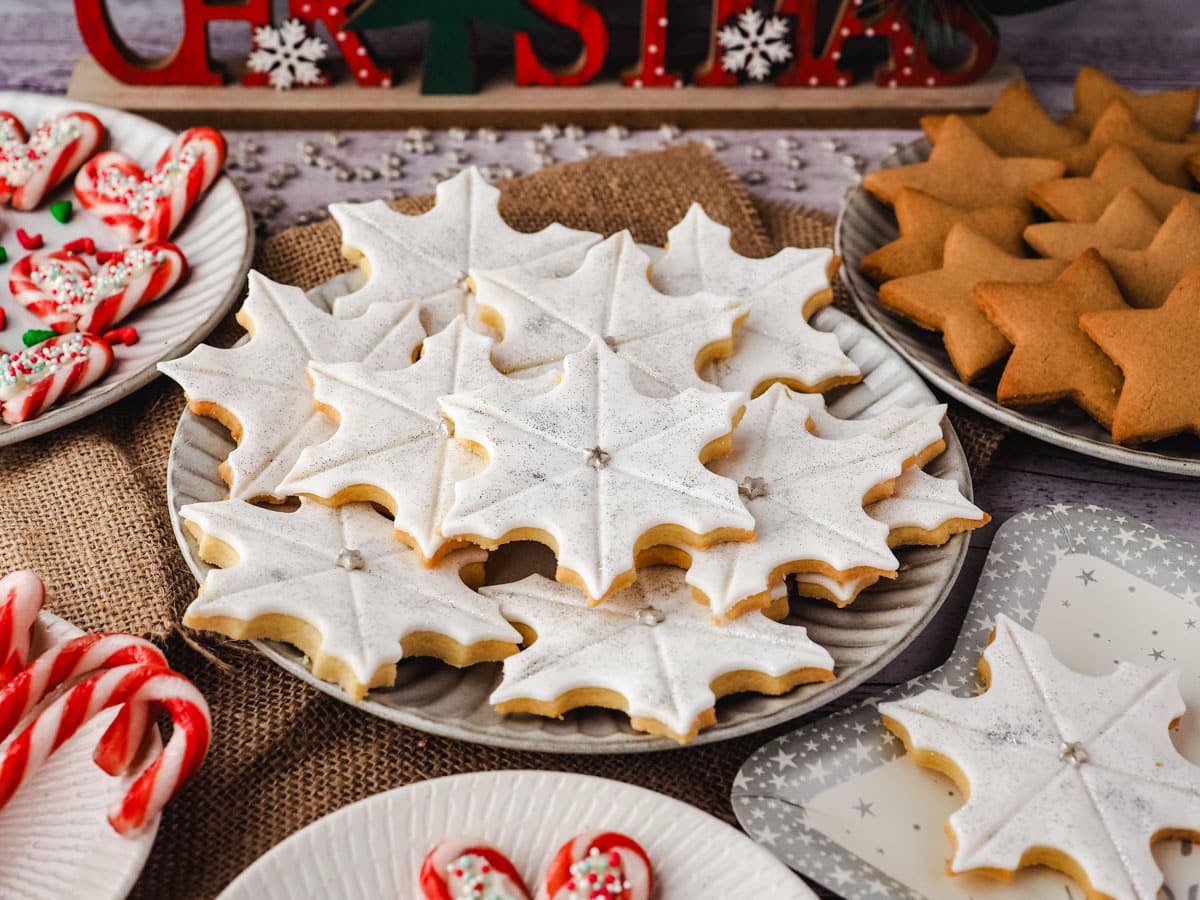 Snowflake cookies on a plate surrounded by Christmas desserts and Christmas decorations.