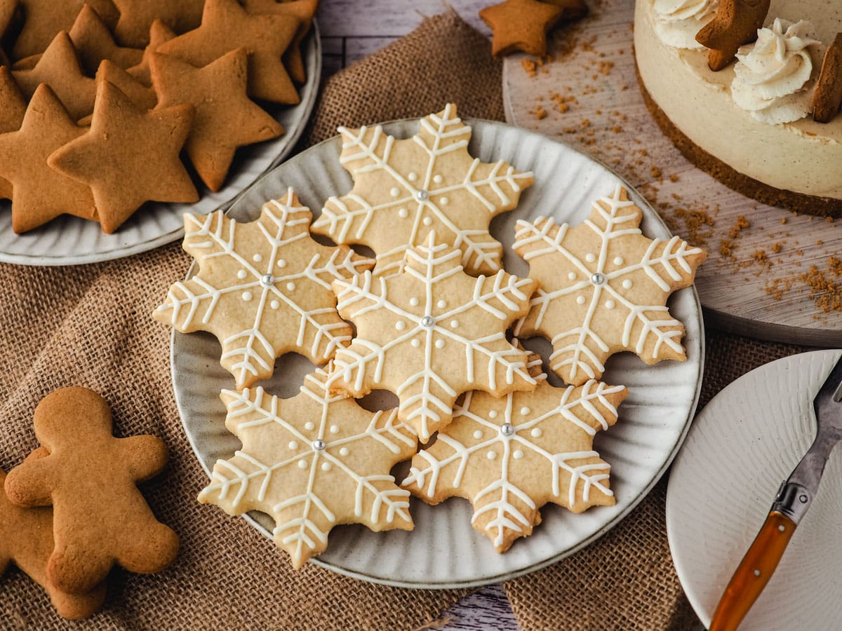 Snowflake cookies on a plate surrounded by Christmas desserts and Christmas decorations.