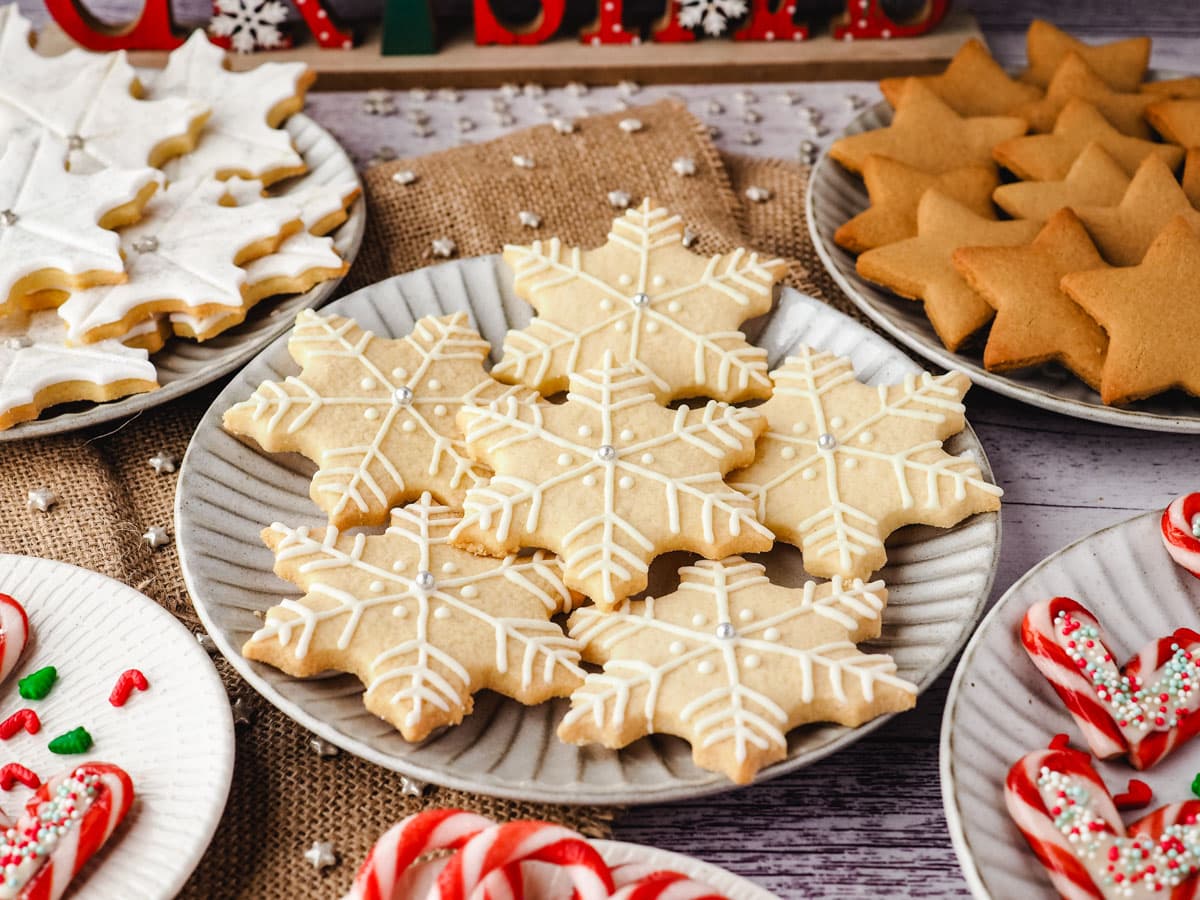 Snowflake cookies on a plate surrounded by Christmas desserts and Christmas decorations.